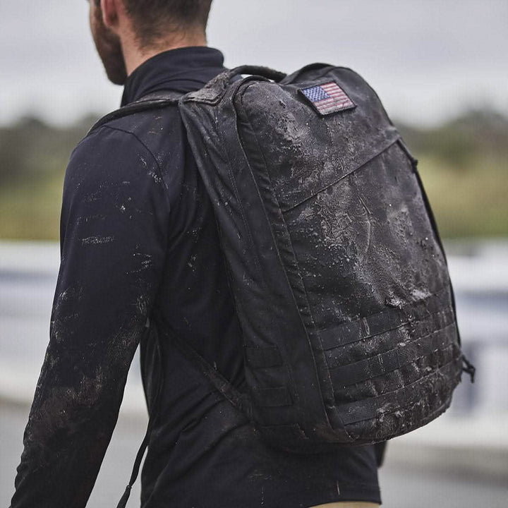 A person outdoors, carrying the GORUCK GR1 USA pack with an American flag patch, showcases the rugged resilience of CORDURA fabric.