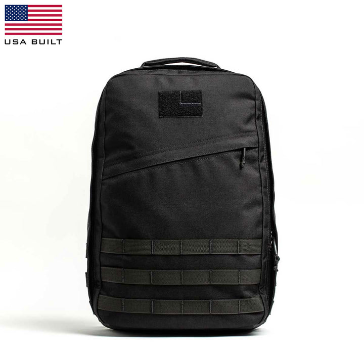 The GR1 USA by GORUCK is a black tactical rucksack highlighted by green MOLLE webbing, made from robust 210D CORDURA. It's displayed against a white backdrop with the USA flag in the top left corner, emphasizing its rugged American craftsmanship.