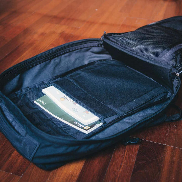 A GR2 - USA rucksack from GORUCK, in black, sits open on the wooden floor, displaying envelopes inside. Its Scars Lifetime Guarantee ensures durability while being carry-on compliant for seamless travel.