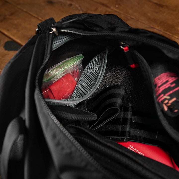 A GORUCK Gym Bag - Ripstop ROBIC® filled with red boxing gloves and gear rests on a wooden floor, showcasing its durable ripstop nylon construction for enhanced toughness.