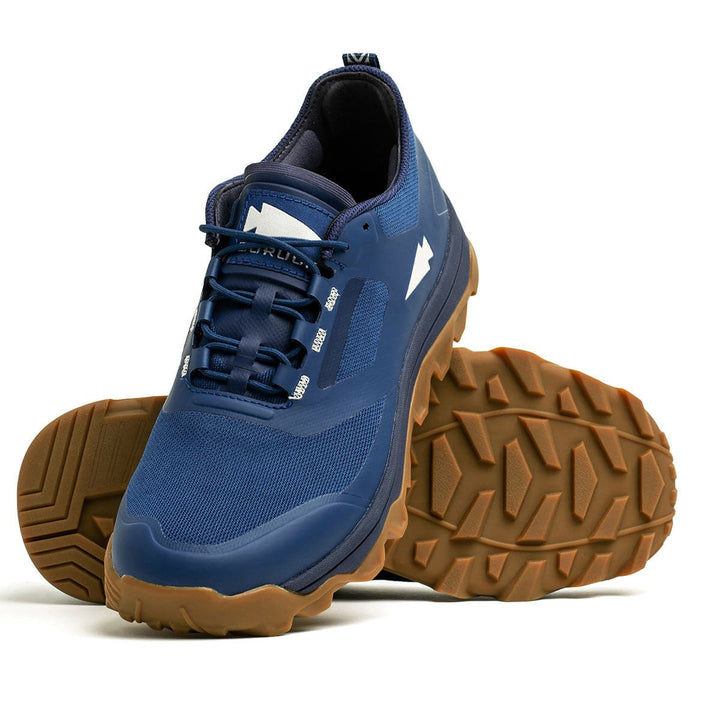 The Mackall - Legion Blue + Gum athletic shoes by GORUCK feature an aggressive triple compound outsole, making them perfect for all-terrain rucking. Inspired by Special Forces training for ultimate durability, one shoe is showcased upright while the other is displayed on its side.