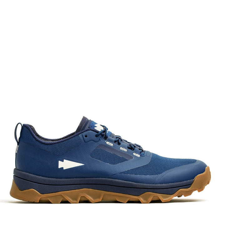 The Mackall in Legion Blue + Gum by GORUCK is a trail running shoe equipped with an aggressive triple compound outsole and gum sole, making it ideal for all-terrain rucking and Special Forces training. It also features an arrow logo on the side, combining style with durability.