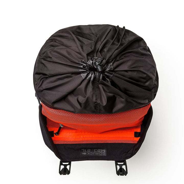 Top view of an open GORUCK M23 - Cordura rucksack with a bright orange interior. This modern rucksack showcases a drawstring closure and sturdy black straps. It's partially open, revealing an orange mesh pocket within, expertly crafted from durable materials to ensure long-lasting use.