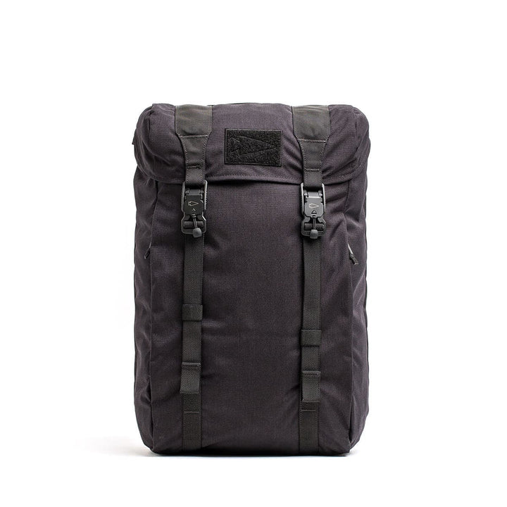 The GORUCK M23 - Cordura is a black backpack featuring a top flap secured with dual buckle straps, crafted from robust materials. It includes a rectangular patch on the flap and showcases a sleek, minimalist design. This sturdy rucksack is spacious, perfect for travel or hiking adventures.