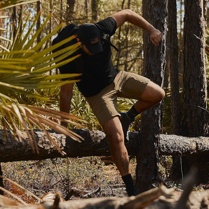 Dressed in outdoor gear, the adventurer navigates over a fallen tree in a sunlit forest, their GORUCK Merino Challenge Socks providing comfort and durability with every step.