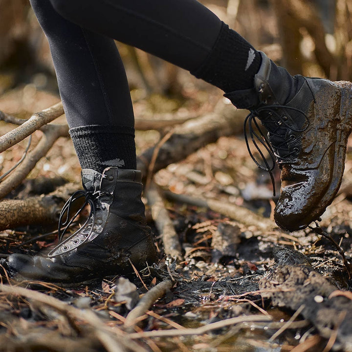 A person trudges through muddy terrain wearing black boots and leggings, their feet kept cozy by GORUCK's warm Merino Challenge Socks.