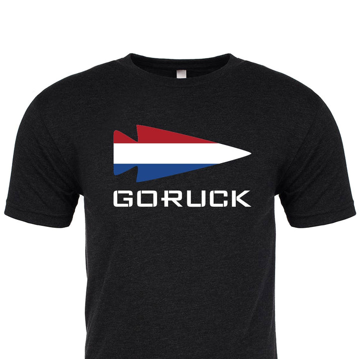 Introducing the "T-shirt - Rep Your Country" by GORUCK EU. This black classic tee showcases a striking red, white, and blue arrow design above the "GORUCK" text. Made from premium tri-blend fabric, it guarantees both comfort and durability, offering timeless style.