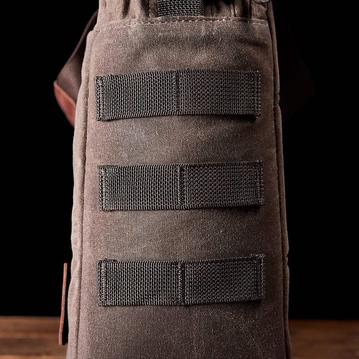 Close-up of a GORUCK Shoulder Bag in waxed canvas, showcasing its rugged texture and MOLLE customization, featuring three horizontal webbing straps on the side against a black background.