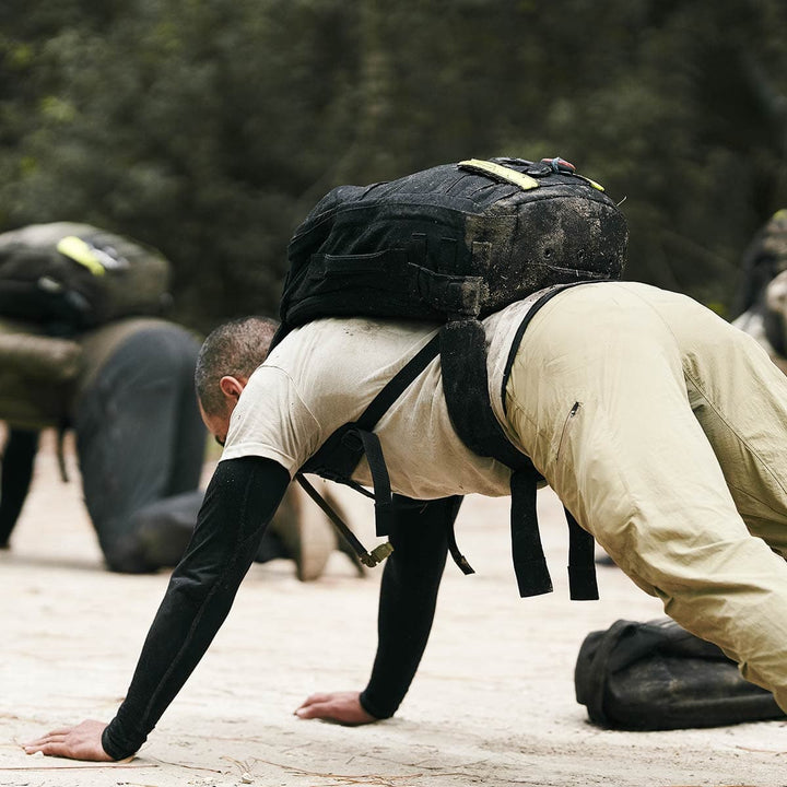 A man performs push-ups outdoors with a rugged GORUCK backpack in a training exercise, its CORDURA fabric ensuring durability.