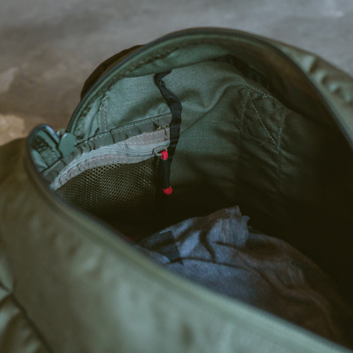 Top view of an open green Kit Bag by GORUCK, revealing gray and green items inside on a textured surface.