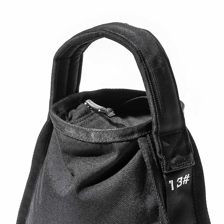 Close-up of a black fabric GORUCK Sand Kettlebells bag, featuring a zipper and handle, highlighting its durable design against a white background. Perfect for securely storing your portable kettlebell.