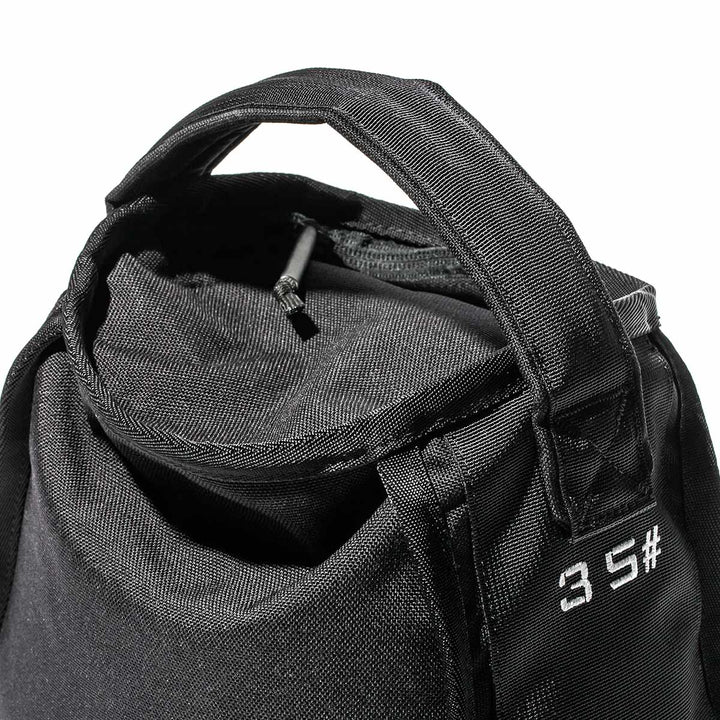 Close-up of a black GORUCK Sand Kettlebell bag featuring a zippered top and short handles, showcasing an endurance design with a white text pattern on the side. Its compact form makes it as portable as a kettlebell, perfect for convenient use on the go.