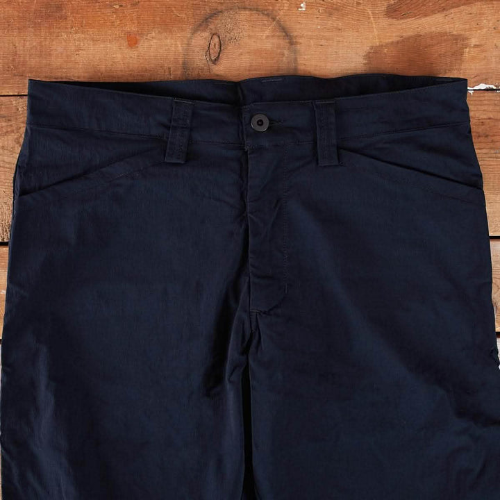 The Men’s Simple Pants - Lightweight ToughDry® by GORUCK, featuring a button closure, are showcased on a wooden surface. Made from ToughDry fabric, they include belt loops and visible stitching along the pockets and waistband for both style and abrasion resistance.