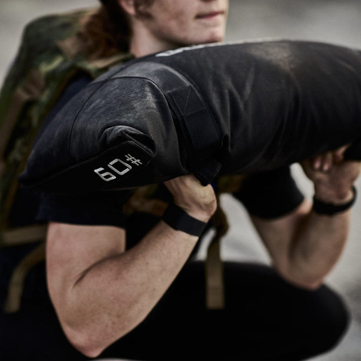 A person incorporating GORUCK's Simple Training Sandbags into their home gym workout lifts a 69-pound sandbag during exercise.