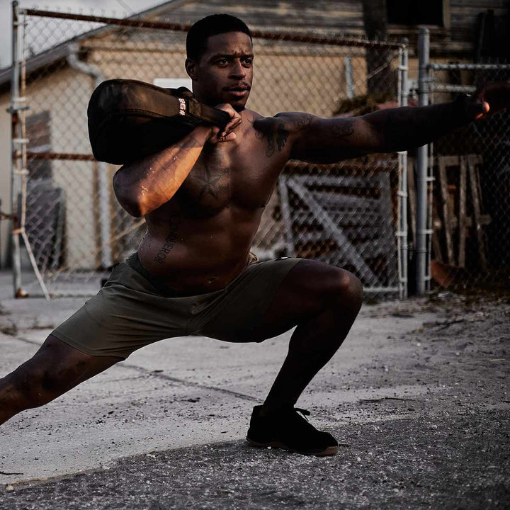 A man is performing an endurance workout outdoors, executing lunges while reaching forward with a Sand Kettlebell from GORUCK.