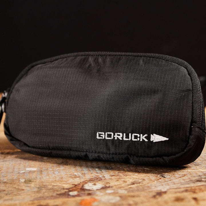 A sleek black GORUCK Belt Bag - Ripstop ROBIC® rests on a wooden surface against a dark background, showcasing the durability of a robust Ripstop Nylon Waist Pack.