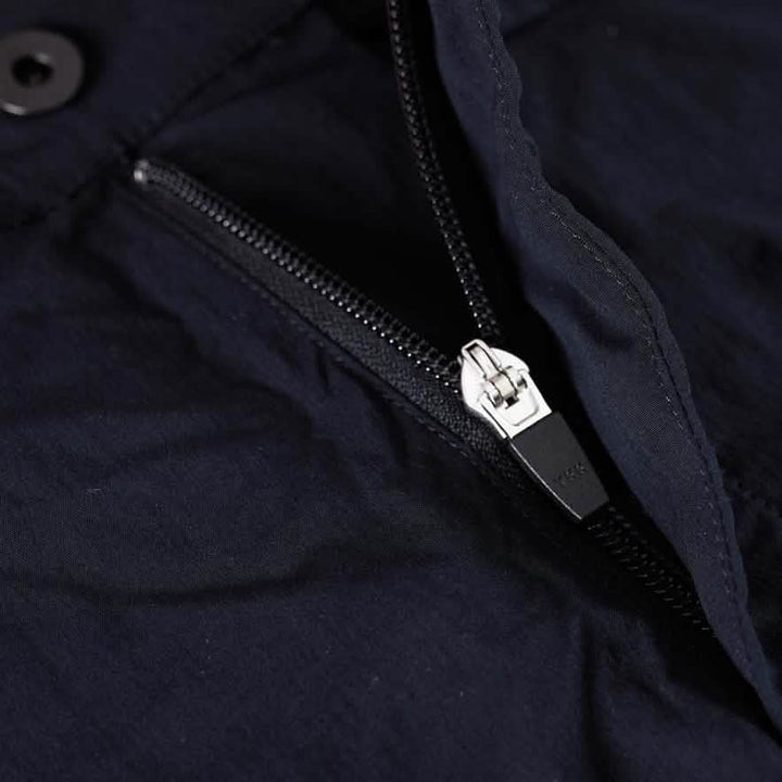 Close-up of a partially unzipped black jacket with a silver metal zipper, crafted from GORUCK's abrasion-resistant material. The smooth, dark fabric contrasts with the black button at the top corner. The zipper is labeled with the GORUCK brand name.